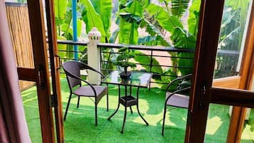 A balcony with a table and chairs, surrounded by lush green foliage.