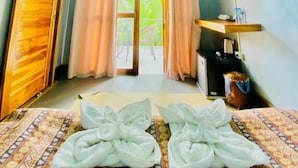 A hotel room with a bed, a desk, a chair, a window with curtains, and an air conditioning unit.