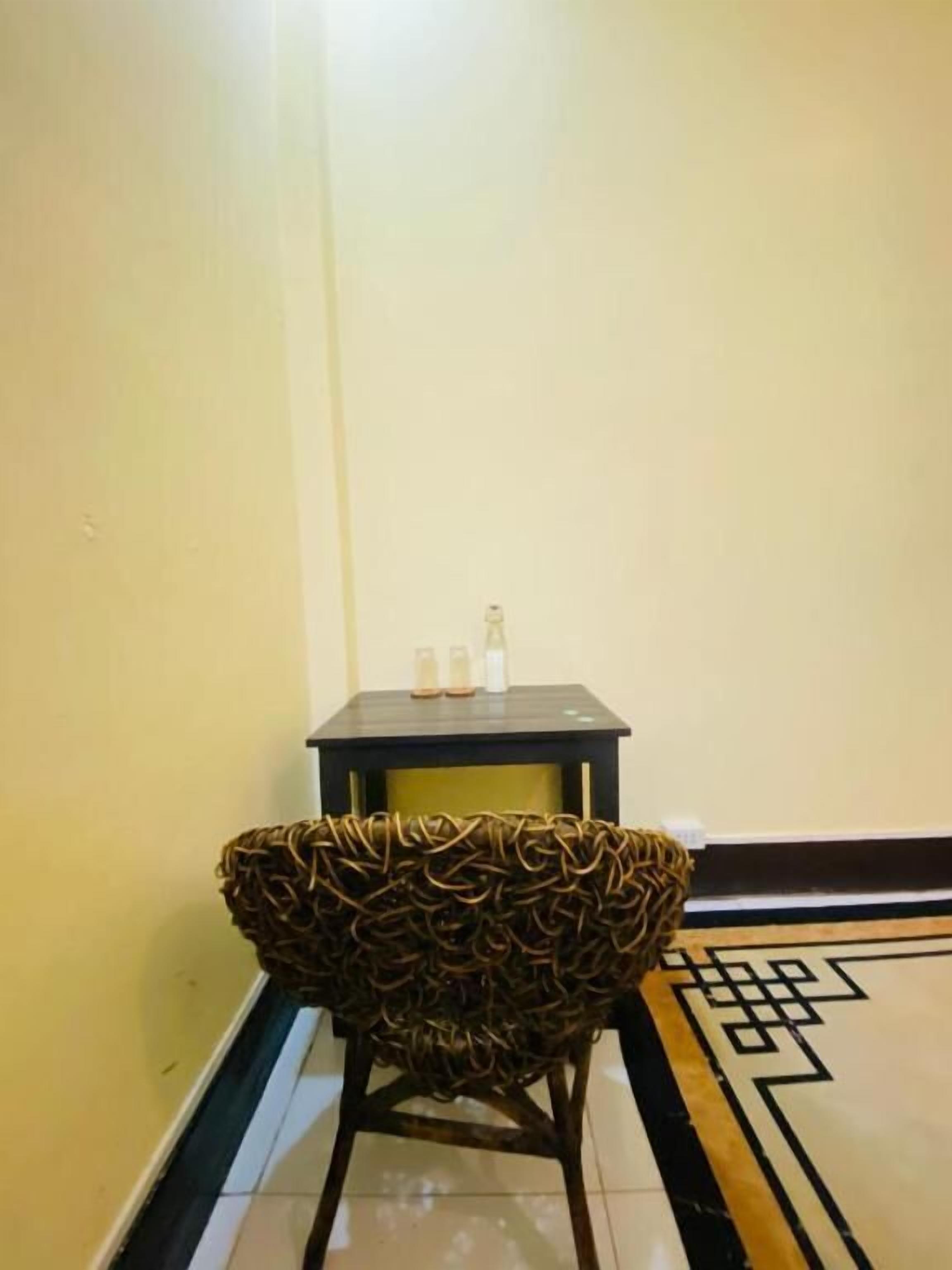 A corner with a woven chair, a small table with bottles, and a patterned floor.