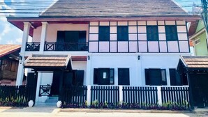 Une maison à deux étages avec un balcon, un porche à l’avant et une clôture en piquets.