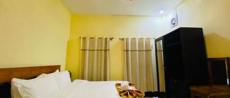 A hotel room with a bed, curtains, a wardrobe, and a ceiling light fixture.