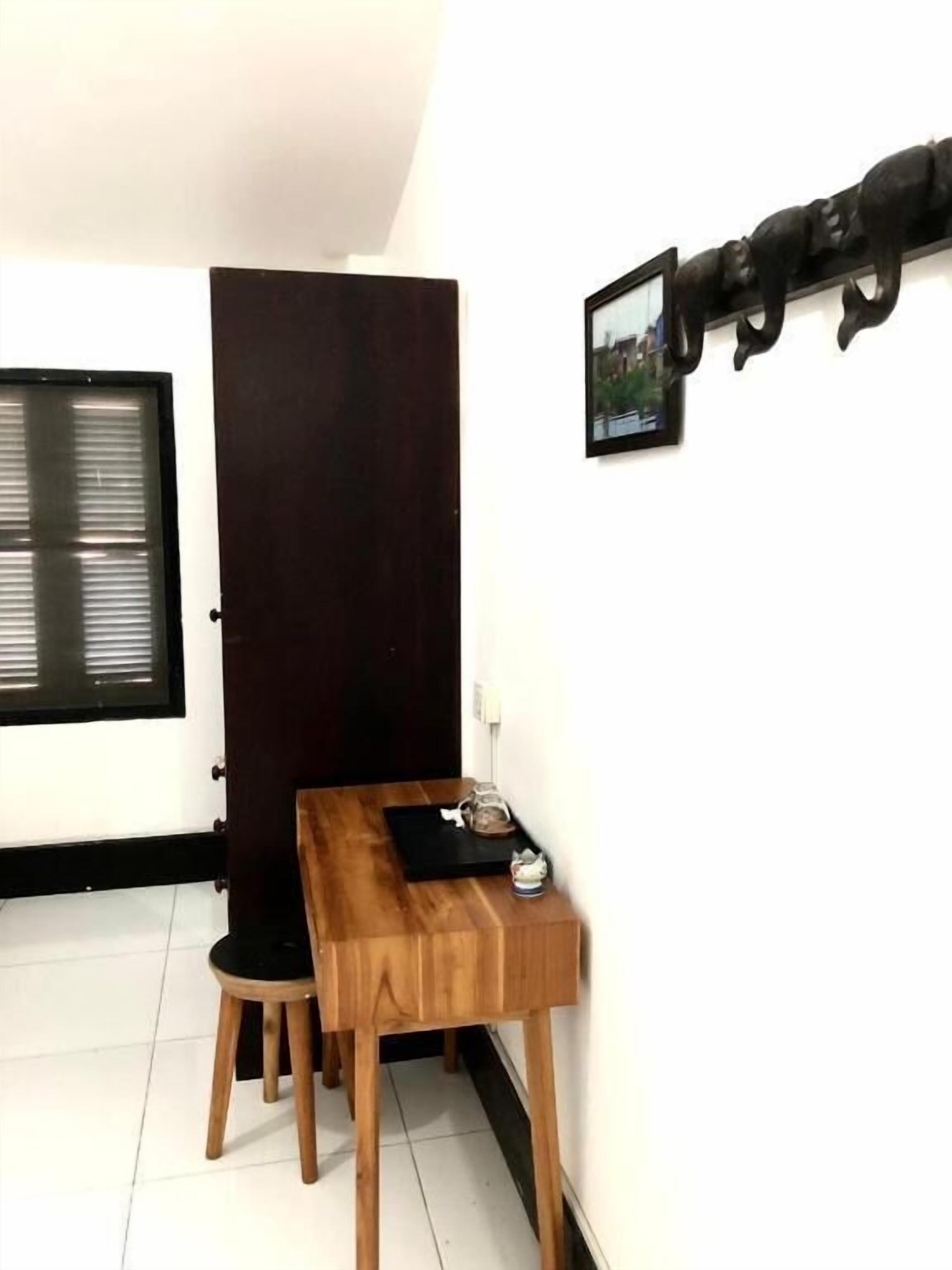 A small dining area with a wooden table and two chairs, a dark door, a window with blinds, and a wall-mounted picture.