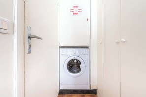 Ein Waschraum mit Waschmaschine, einer Tür mit Sicherheitsschild und einem Lichtschalter.