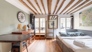 Ein Schlafzimmer mit Holzboden, einem Bett mit gemusterten Kissen, einem Schreibtisch mit Lampen und einer großen Wanduhr.