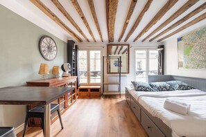 Ein Schlafzimmer mit Holzboden, einem Bett mit gemusterten Kissen, einem Schreibtisch mit Lampen und einer großen Wanduhr.