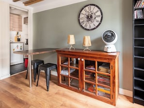 Una cucina con un tavolo di legno, due sgabelli, una sveglia, una ventola e una libreria.