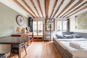 A room with a wooden ceiling, a bed with patterned pillows, a desk with lamps, and a large wall clock. - Central Parisian-style Studio Apart - Sentier (Paris)