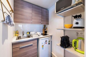 A compact kitchen with a sink, a refrigerator, and a microwave on a shelf.