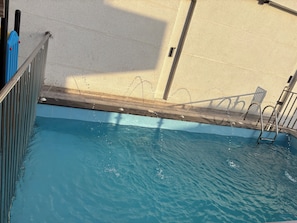 A swimming pool with a metal ladder, a tiled deck, and a concrete wall.