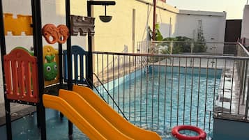 A swimming pool with a yellow slide, a red lifebuoy, and a metal fence.