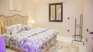 A bedroom with a bed, a bedside table with a lamp, a window, and a wall-mounted ladder.