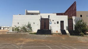 A modern building with a flat roof, a large entrance with steps, and a unique triangular structure on the right.