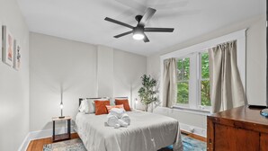 A bedroom with a bed, a ceiling fan, a window with curtains, a bedside table with a lamp, and a wooden dresser. - Charming Garden Home in Old Louisville (Louisville)