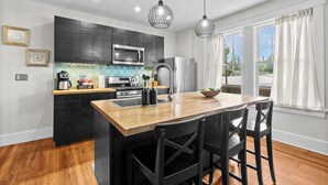 A modern kitchen with a central island, black cabinets, stainless steel appliances, and pendant lighting. - Charming Garden Home in Old Louisville (Louisville)