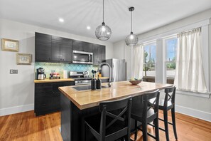 A modern kitchen with a central island, black cabinets, stainless steel appliances, and pendant lighting. - Charming Garden Home in Old Louisville (Louisville)