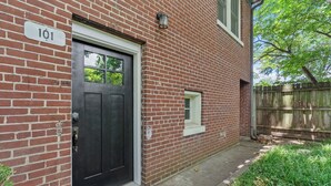 A brick building with a black door, a small window, and a wooden fence in the background. - Charming Garden Home in Old Louisville (Louisville)