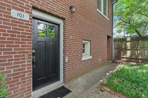 A brick building with a black door, a small window, and a wooden fence in the background. - Charming Garden Home in Old Louisville (Louisville)