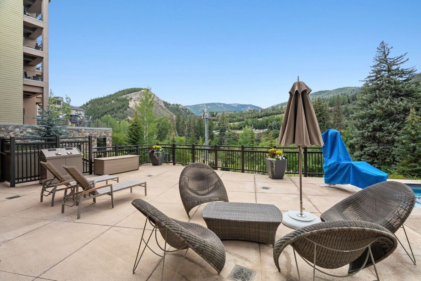 A patio with wicker furniture, a grill, and a view of mountains.