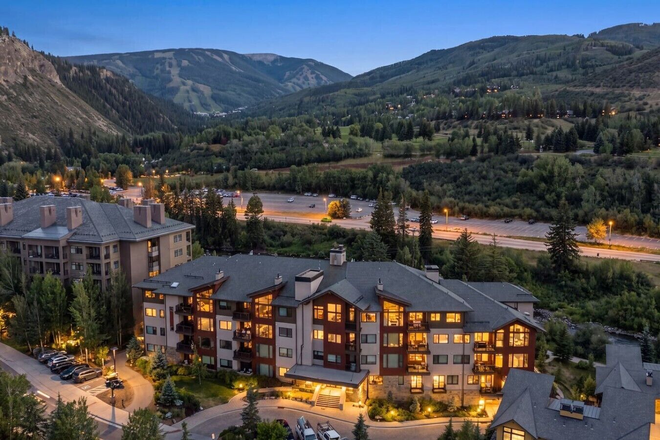 A multi-story hotel with a modern design, located in a mountainous area with a view of the valley and a road in the foreground.