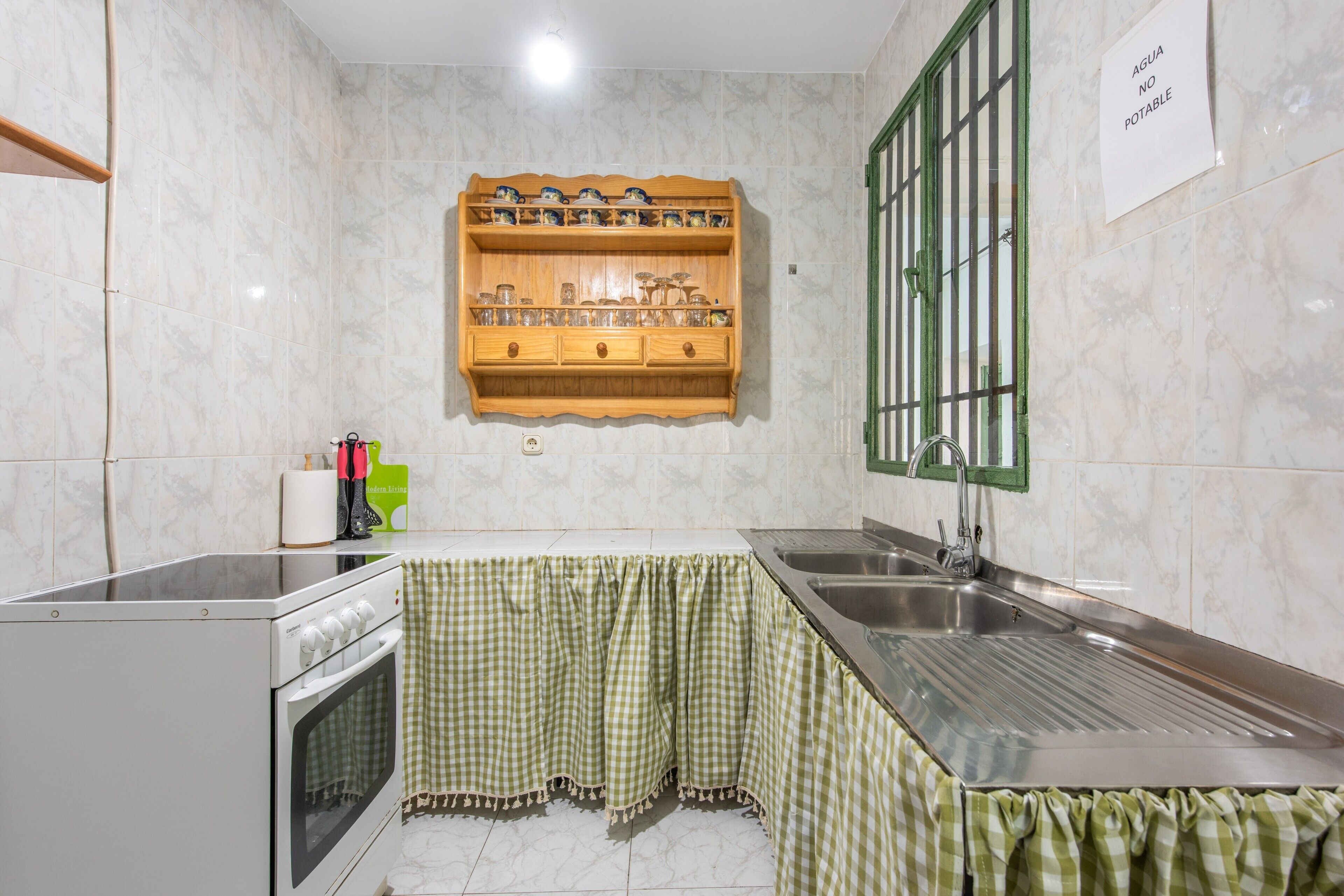 Une cuisine avec une étagère en bois au-dessus du plan de travail, un évier, un four et une nappe à carreaux verts.