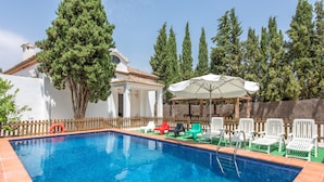 Una piscina con borde de azulejos, rodeada por una valla de madera y un edificio blanco con tejado de cerámica.