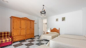 Una habitación con piso a cuadros, un armario de madera, un sofá rojo y dos camas con ropa blanca.