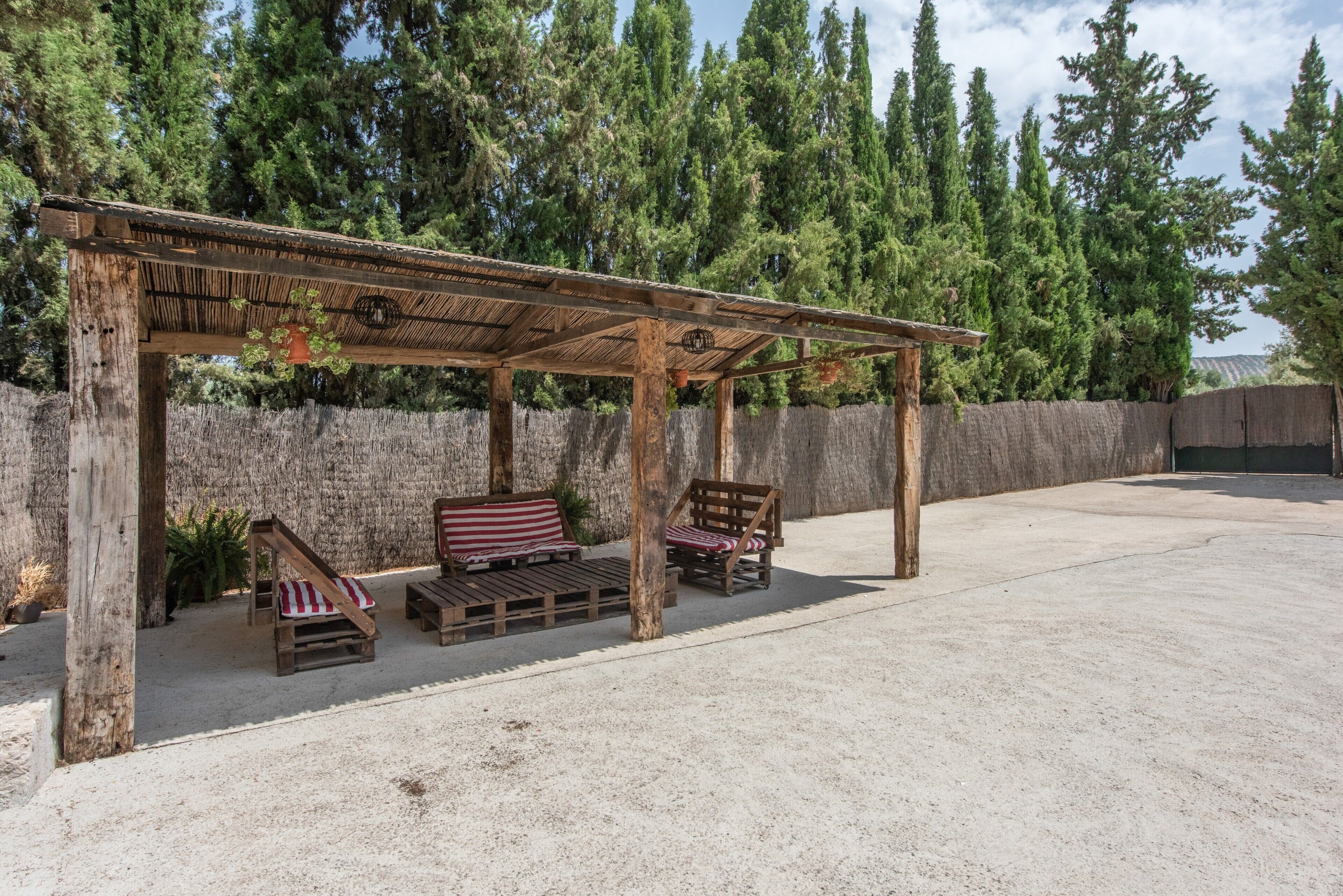 Une pergola en bois avec des sièges, un mur en pierre et une vue sur de grands arbres.