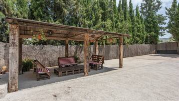 Une pergola en bois avec des sièges, un mur en pierre et une vue sur de grands arbres.