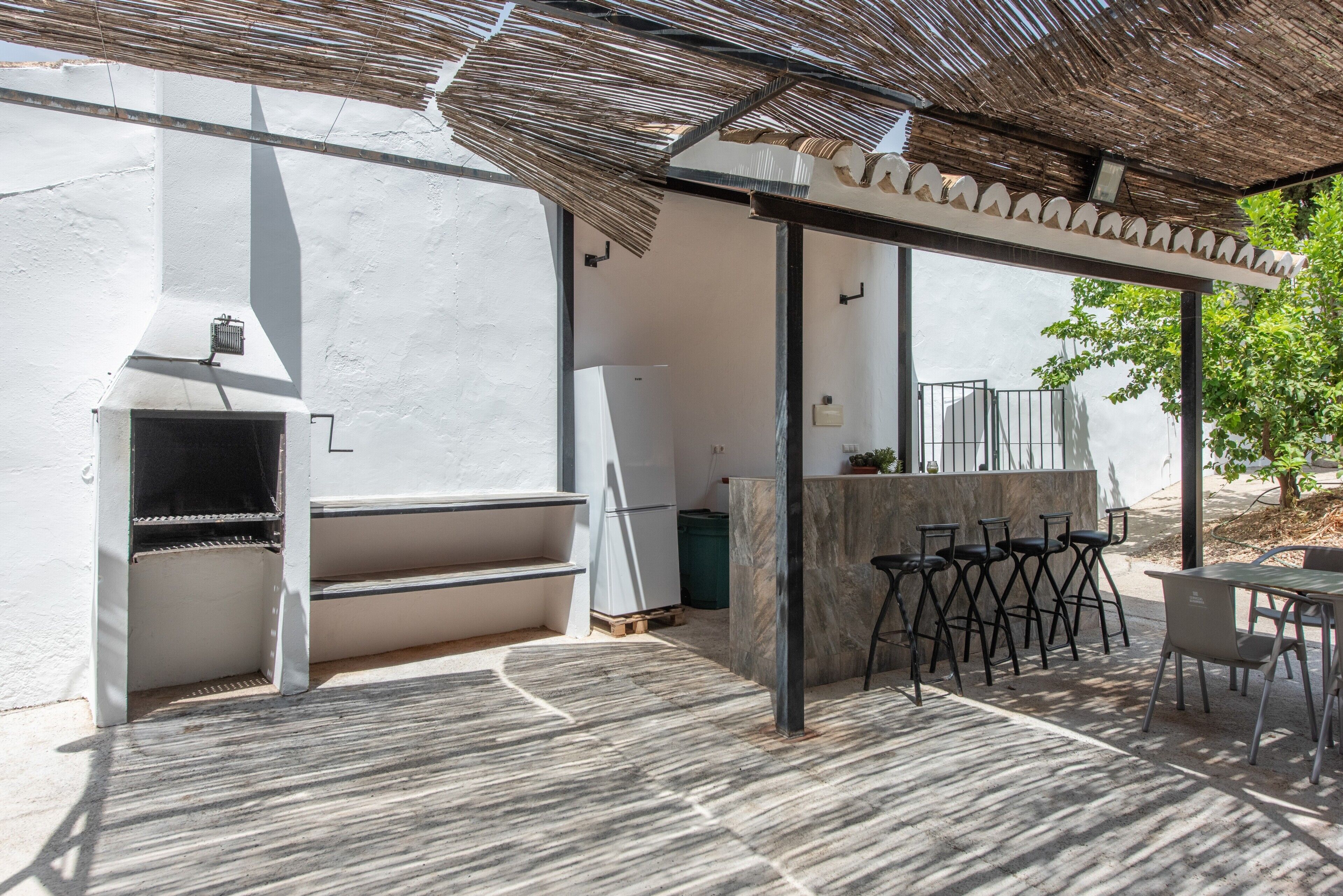 Un patio exterior con una parrilla, zona de estar y una pérgola que ofrece sombra.