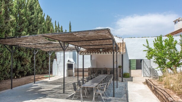 Un patio exterior con pérgola, una mesa larga y sillas.