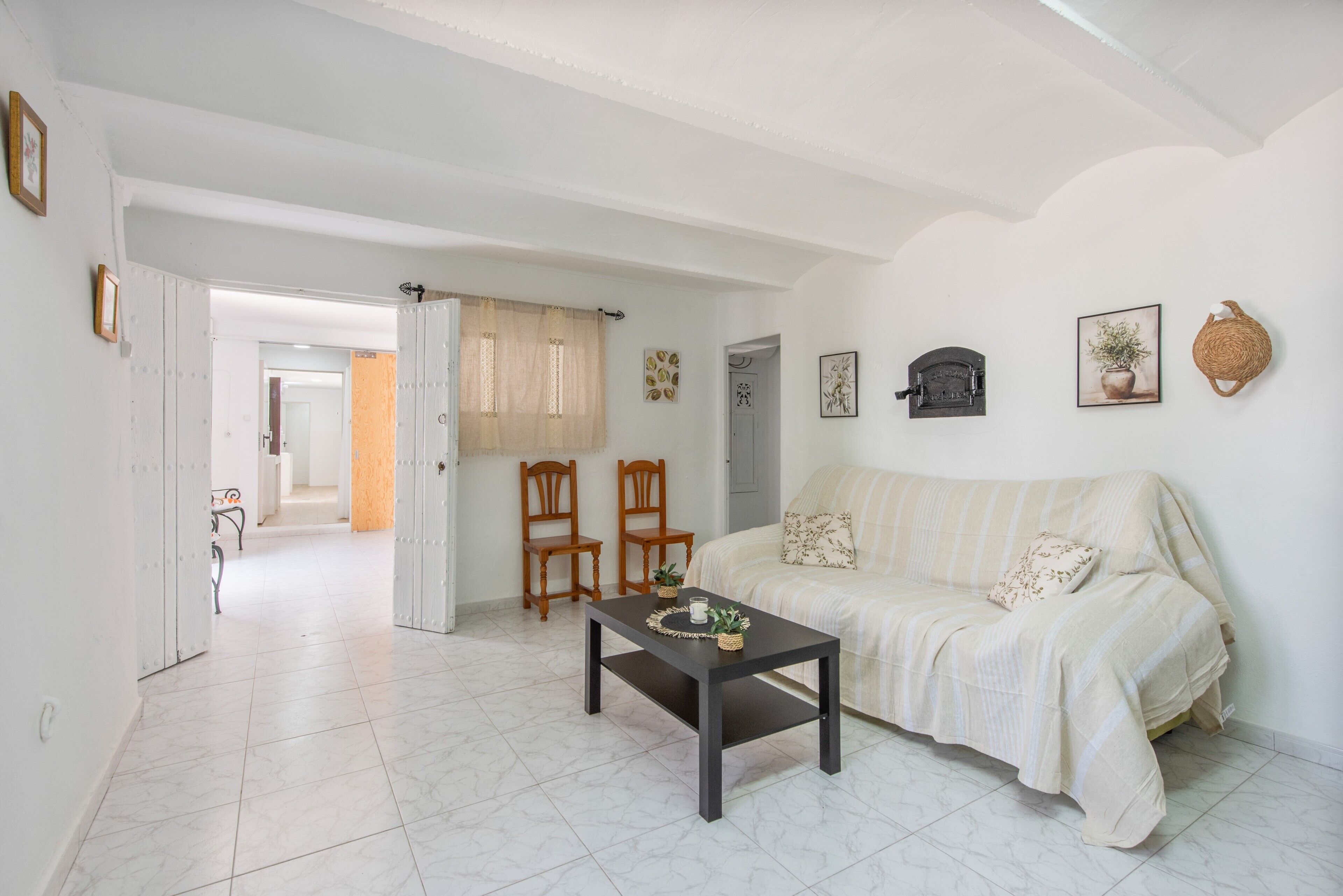 Un salón con un sofá, dos sillas de madera, una mesa de centro y una puerta que da a otra habitación.