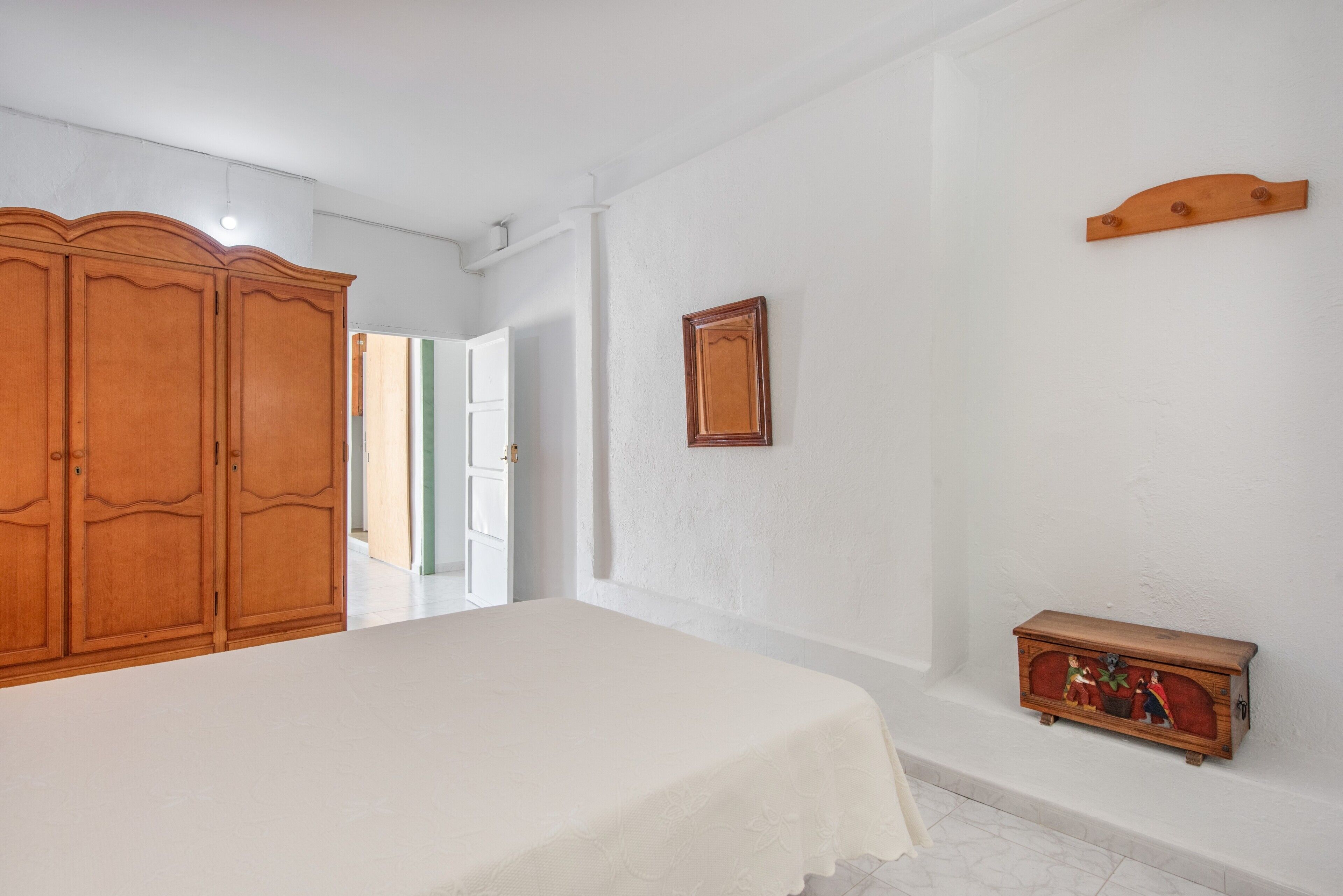 Un dormitorio con cama, armario de madera, pequeño mueble de madera y puerta que da a otra habitación.