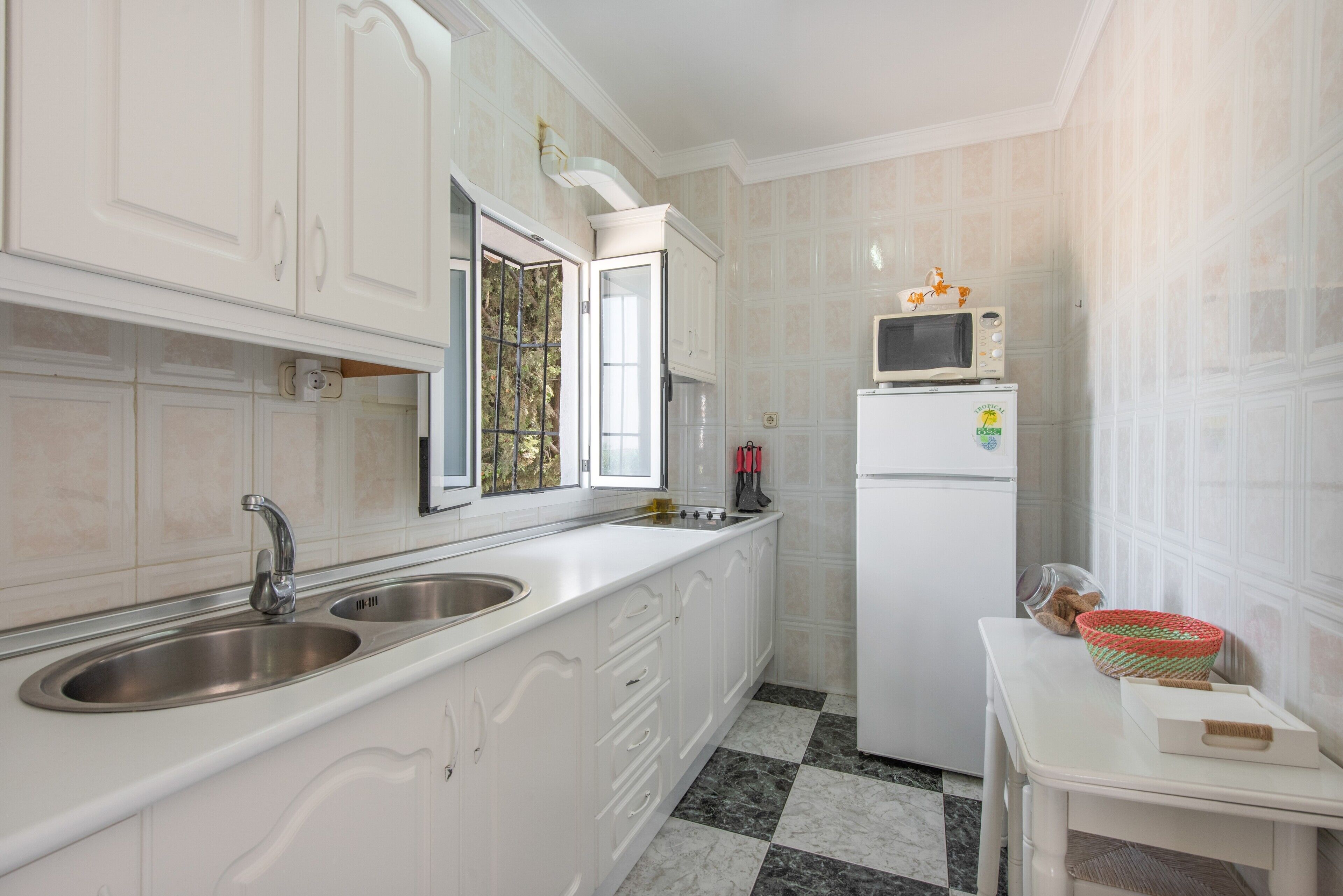 A kitchen with white cabinetry, a double sink, a microwave, and a refrigerator.