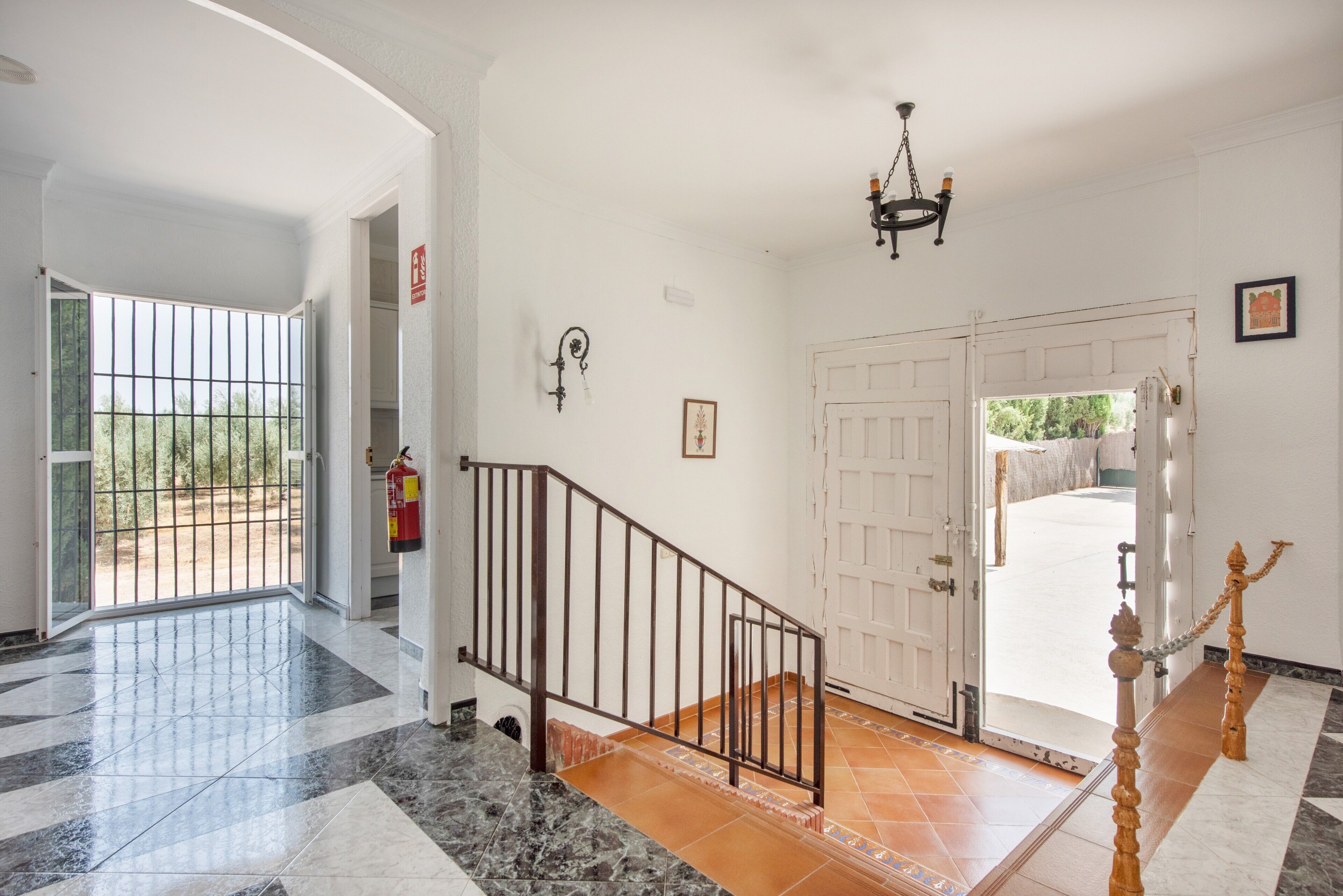 A spacious hallway with a marble floor, a staircase with a metal railing, and a white door leading outside.