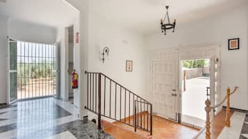 A spacious hallway with a marble floor, a staircase with a metal railing, and a white door leading outside.