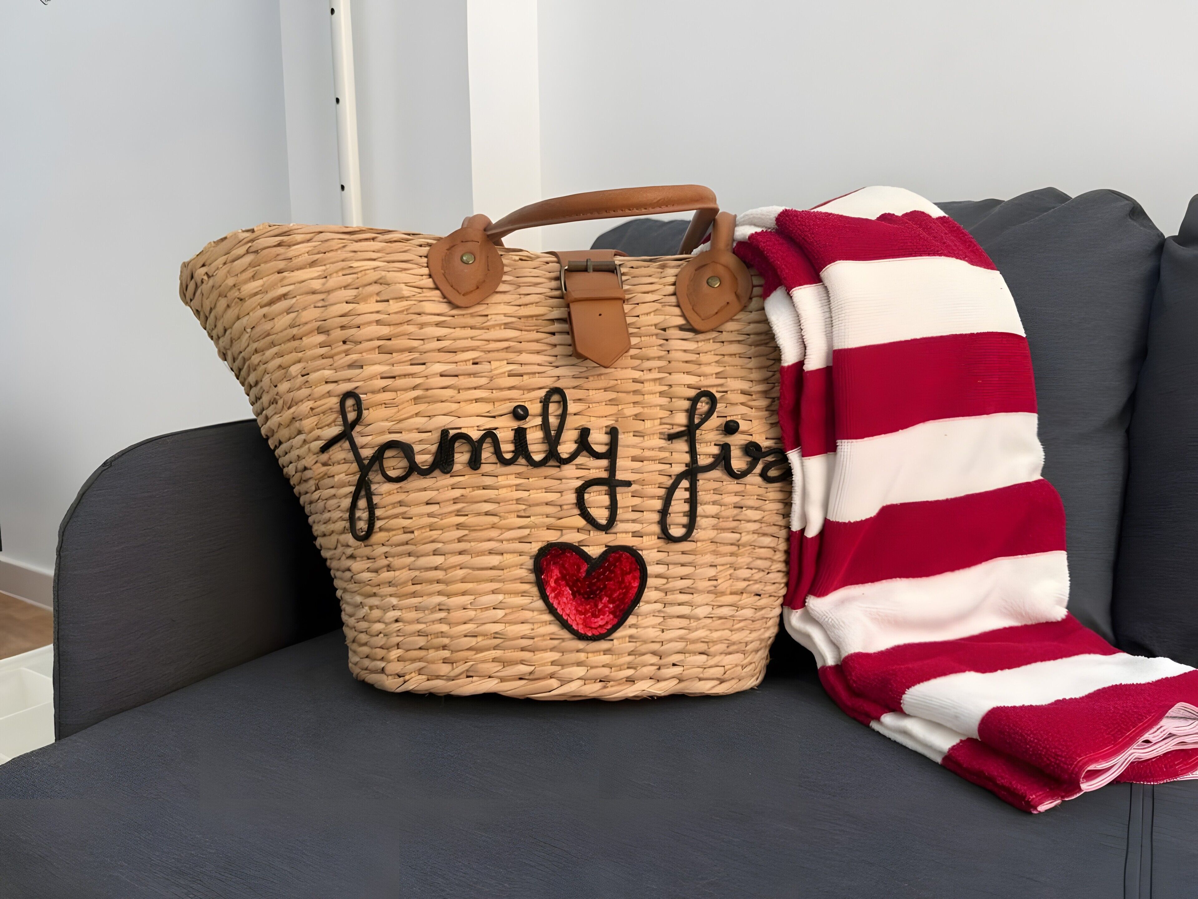 Un bolso de tela tejido con el texto 'family first' bordado, colocado junto a una manta a rayas sobre un sofá gris.