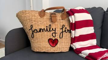 Un bolso de tela tejido con el texto 'family first' bordado, colocado junto a una manta a rayas sobre un sofá gris.