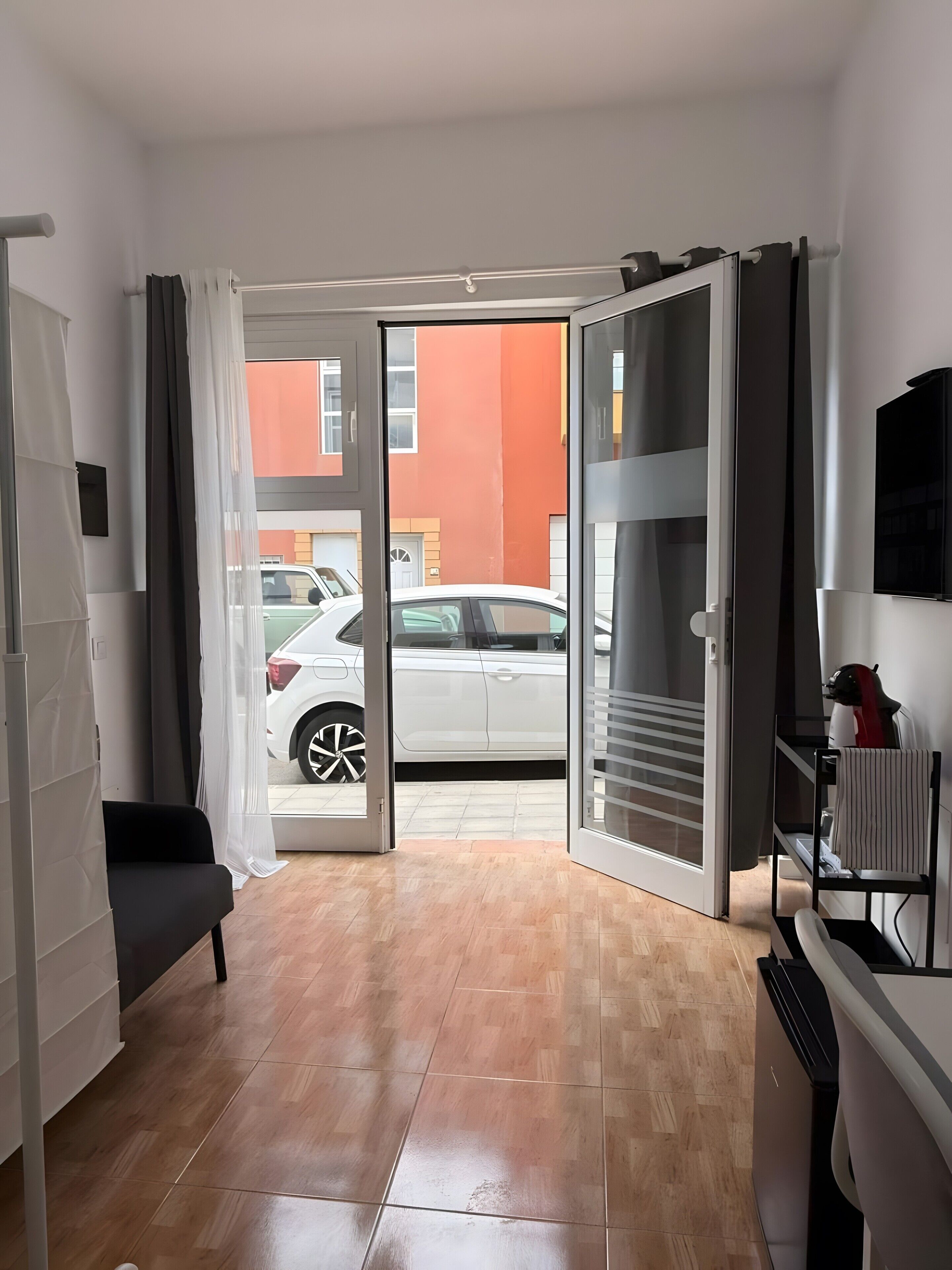 Ein Zimmer mit einer Schiebetür zum Parkplatz, einem schwarzen Stuhl und einem an der Wand montierten Fernseher.