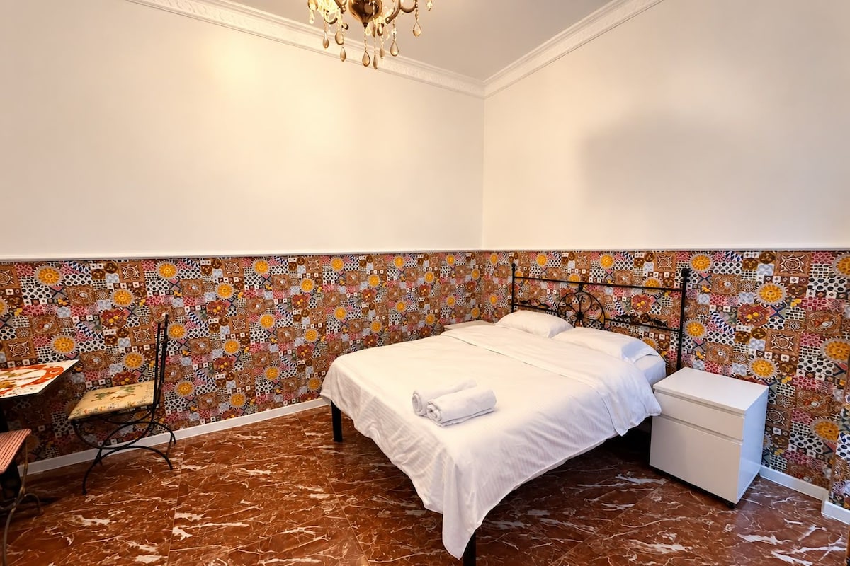 A hotel room with a bed, bedside table, and a desk with a chair.