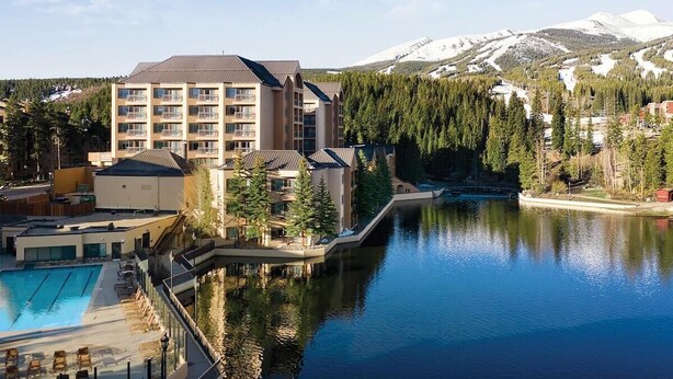 Un hotel con piscina, montañas al fondo y un lago.