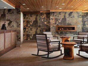 A lobby with a stone wall, wooden ceiling, and seating area with patterned chairs and a central wooden table. - Studio Villa at Marriott Mountain Valley Lodge (Breckenridge)