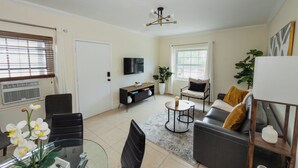 Uma sala de estar moderna com sofá, mesa de centro, cadeiras, televisão de tela plana e um vaso de planta.