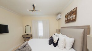 Quarto de hotel com cama, mesa de cabeceira, luminária, ar condicionado e um quadro na parede.