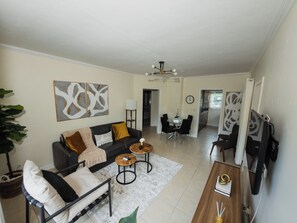 A living room with a sofa, coffee table, and a dining area with chairs. - Chic Wynwood Getaway–Steps to Wynwood & Midtown (Miami)