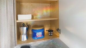 Um armário de cozinha com uma cafeteira, um recipiente de café Maxwell House e um jarro azul para água.