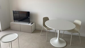 Una camera moderna con una TV a schermo piatto su un mobile bianco, un tavolo rotondo con due sedie e un condizionatore d'aria a parete.