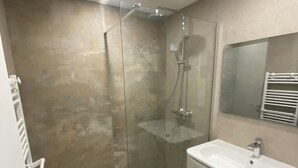 Un bagno moderno con doccia vetro, lavandino bianco e specchio sopra il lavandino.