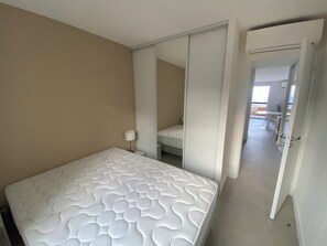 Ein Schlafzimmer mit einem Bett, einer Nachttischlampe, einer Schiebetür, die zu einem Balkon führt, und Blick auf den Balkon.