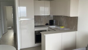 Una cucina moderna con mobili bianchi, forno integrato, macchina da caffè e lavello.