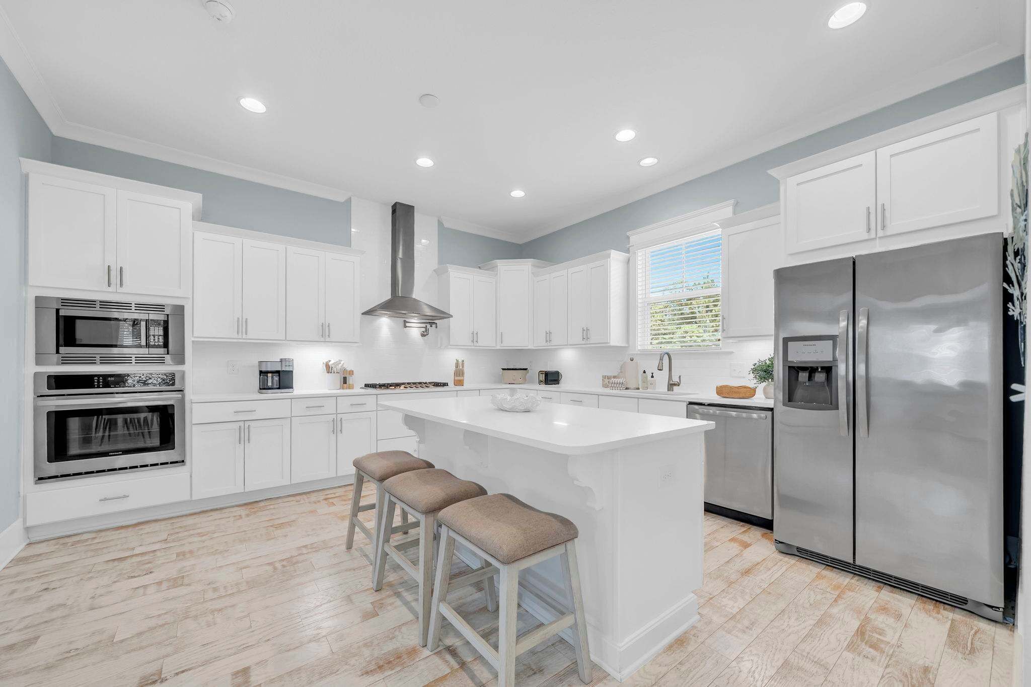 A modern kitchen with white cabinetry, stainless steel appliances, a central island with stools, and a large refrigerator.